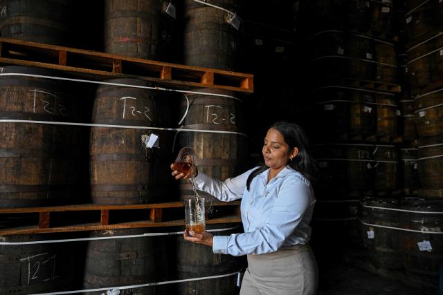 A worker takes a rum sample from barrels stored in an aging warehouse at the Santa Teresa rum factory in La Victoria, Aragua state, Venezuela, on December 17, 2025. (Photo by Federico PARRA / AFP)
