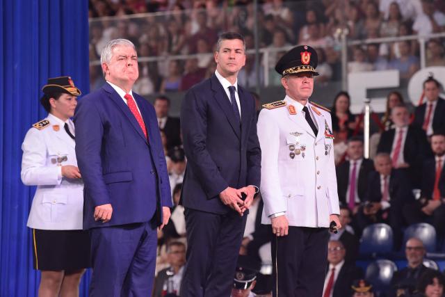 Paraguay's President Santiago Pena (C), Interior Minister Enrique Riera Escudero (L) and National Police Commander Carlos Benitez attend the graduation ceremony of nearly 5,000 new noncommissioned officers of the National Police at the Ueno Defensores del Chaco stadium in Asuncion on December 18, 2025. The ceremony included the symbolic awarding of diplomas, the oath of the new noncommissioned officers, and messages from the main national authorities. (Photo by DANIEL DUARTE / AFP)