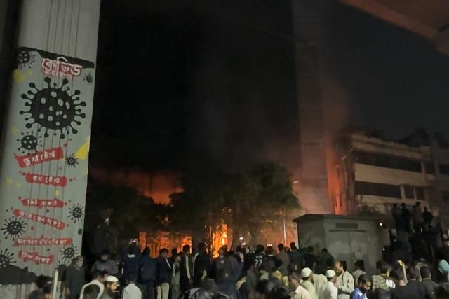This frame grab from AFPTV video footage taken on December 19, 2025 shows people gathering near a fire outside the Daily Star office in Dhaka, amid protests following the news of the death of youth leader Sharif Osman Hadi. Violence broke out in Bangladesh's capital early December 19 after a youth leader of the country's 2024 pro-democracy uprising who was injured in an assassination attempt died in a hospital in Singapore. Several buildings in the capital, including those housing the country's two leading newspapers, were set on fire, according to authorities, with staff trapped inside. (Photo by Maruf Hasan / AFPTV / AFP)