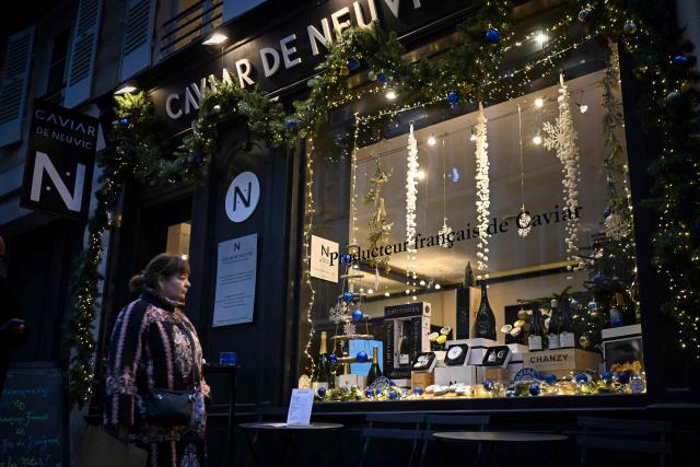 A pedestrian looks at the store window of the Caviar de Neuvic boutique in Paris on December 11, 2025. A pioneer in Bulgarian caviar production has to go the extra mile ahead of the festive season to whet appetites for his beluga caviar, striving to meet demand from all over the world, as November and December are the busiest months for Mateev on the southern Bulgarian Kardzhali lake in the heart of the Rhodope Mountains, the alleged birthplace of the mythical Orpheus. (Photo by Nikolay DOYCHINOV / AFP)