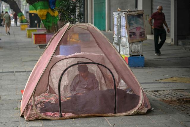 A homeless woman sits under a mosquito tent along a pavement on a winter morning in Chennai on December 19, 2025. (Photo by R.Satish BABU / AFP)