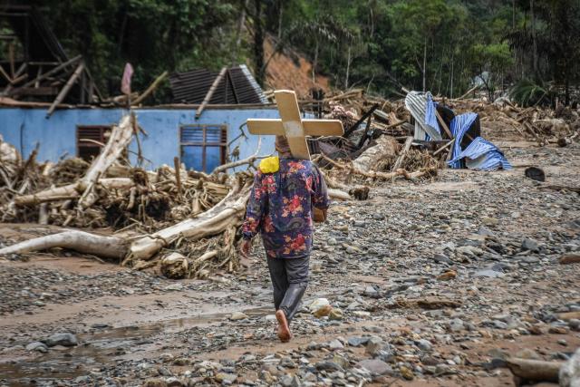 A man carrying a cross walks in front of search and rescue members as they carry a coffin amid the relocation of the graves of flash flood victims along a riverbank where a flash flood struck about three weeks earlier, in Hutanabolon, North Sumatra, on December 18, 2025. The latest government figures issued on December 16 put the death toll of the devastating floods at 1,030 people. Another 205 remain missing in the aftermath of one of the deadliest natural disasters to hit Sumatra's resource-rich Aceh province, the scene of a killer tsunami in 2004. (Photo by Damai Mendrofa / AFP)