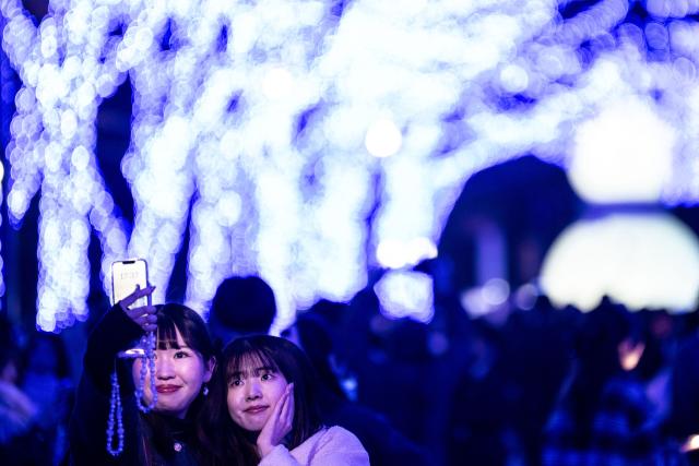 People take pictures with festive light installations ahead of Christmas in Tokyo's Shibuya district on December 19, 2025. (Photo by Philip FONG / AFP)