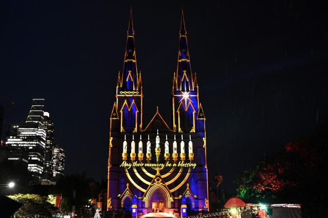 Sydney’s St. Mary’s Cathedral is illuminated with a menorah during a light show on December 19, 2025, in tribute to victims of the Bondi attack. A young girl and Holocaust survivors were among 15 people shot and killed allegedly by a father and his son at a Jewish Hanukkah festival gathering on Australia's Bondi Beach. (Photo by Saeed KHAN / AFP)