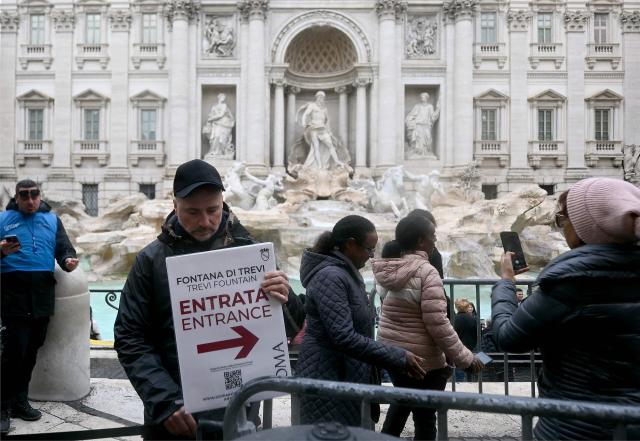 A man holds a placard reading "Entrance" in front of the Trevi fountain in central Rome on December 19, 2025. (Photo by Filippo MONTEFORTE / AFP)
