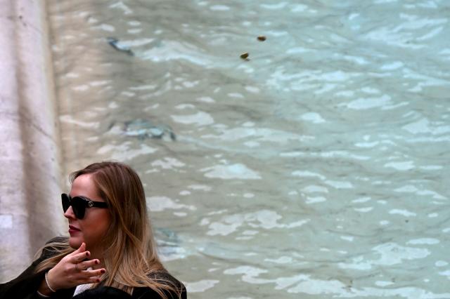 A woman throws coins inside the pool as she visits the Trevi fountain in central Rome on December 19, 2025. (Photo by Filippo MONTEFORTE / AFP)