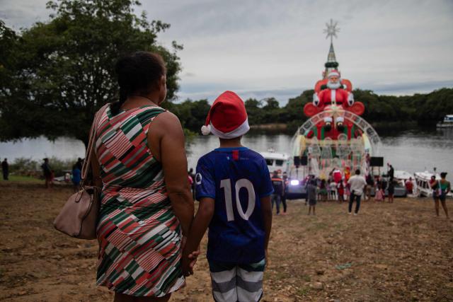 A child and a woman watch the arrival of a ferry decorated for Christmas in the community of Bela Vista do Jaraqui, on the Rio Negro, in the rural area of Manaus, Amazonas state, northern Brazil on December 18, 2025. ‘Natal nas Aguas’ (Christmas on the Waters) is an initiative that brings the magic of Christmas to riverside communities in hard-to-reach locations. (Photo by MICHAEL DANTAS / AFP)