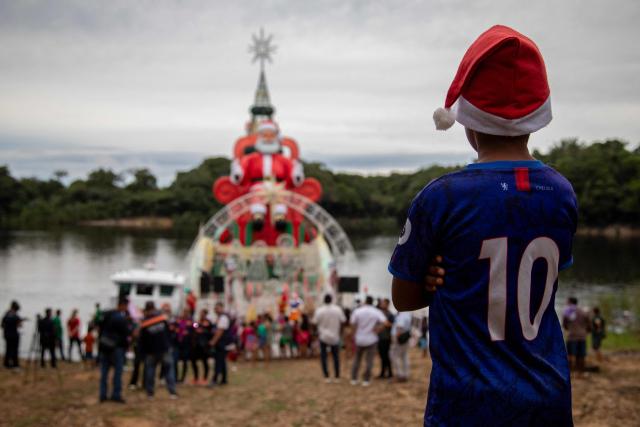 TOPSHOT - A child watches the arrival of a ferry decorated for Christmas in the community of Bela Vista do Jaraqui, on the Rio Negro, in the rural area of Manaus, Amazonas state, northern Brazil on December 18, 2025. ‘Natal nas Aguas’ (Christmas on the Waters) is an initiative that brings the magic of Christmas to riverside communities in hard-to-reach locations. (Photo by MICHAEL DANTAS / AFP)