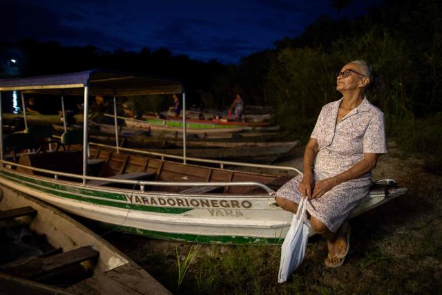 A woman watches the arrival of a ferry decorated for Christmas in the community of Bela Vista do Jaraqui, on the Rio Negro, in the rural area of Manaus, Amazonas state, northern Brazil on December 18, 2025. ‘Natal nas Aguas’ (Christmas on the Waters) is an initiative that brings the magic of Christmas to riverside communities in hard-to-reach locations. (Photo by MICHAEL DANTAS / AFP)