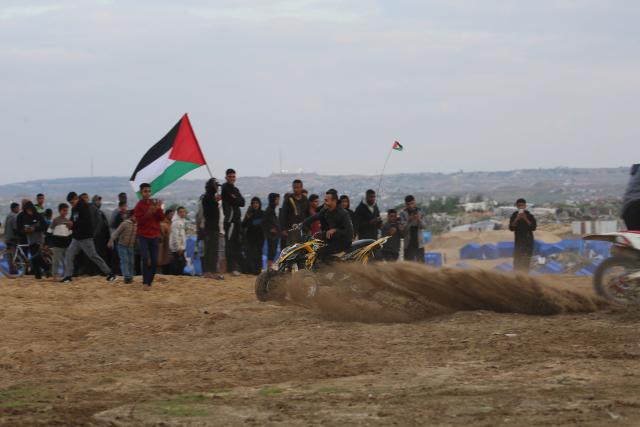 Displaced Palestinians watch as a motorcyclist rides on the sand dunes opposite displacement shelters in Nuseirat camp in the central Gaza Strip on December 19, 2025. A famine declared in Gaza in August is now over thanks to improved access for humanitarian aid, the United Nations said on December 19, but warned the food situation in the Palestinian territory remained dire. More than 70 percent of the population is living in makeshift shelters, it said, with hunger exacerbated by winter floods and an increasing risk of hypothermia as temperatures plummet. Although a ceasefire between Israel and militant group Hamas that took effect in October has partially eased restrictions on goods and aid, delivery fluctuates daily and is limited and uneven across the territory, it said. (Photo by Eyad Baba / AFP)