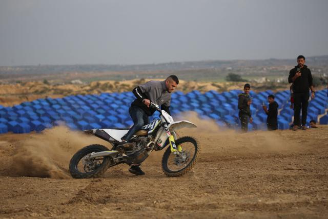 Displaced Palestinians watch as a motorcyclist rides on the sand dunes opposite displacement shelters in Nuseirat camp in the central Gaza Strip on December 19, 2025. A famine declared in Gaza in August is now over thanks to improved access for humanitarian aid, the United Nations said on December 19, but warned the food situation in the Palestinian territory remained dire. More than 70 percent of the population is living in makeshift shelters, it said, with hunger exacerbated by winter floods and an increasing risk of hypothermia as temperatures plummet. Although a ceasefire between Israel and militant group Hamas that took effect in October has partially eased restrictions on goods and aid, delivery fluctuates daily and is limited and uneven across the territory, it said. (Photo by Eyad Baba / AFP)