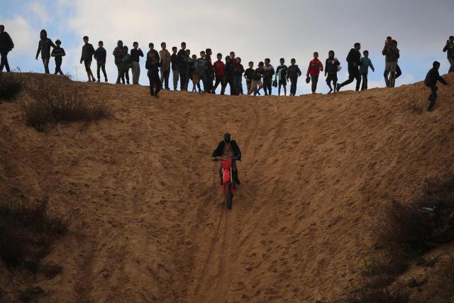 Displaced Palestinians watch as a motorcyclist rides on the sand dunes opposite displaced shelters in Nuseirat camp in the central Gaza Strip on December 19, 2025. A famine declared in Gaza in August is now over thanks to improved access for humanitarian aid, the United Nations said on December 19, but warned the food situation in the Palestinian territory remained dire. More than 70 percent of the population is living in makeshift shelters, it said, with hunger exacerbated by winter floods and an increasing risk of hypothermia as temperatures plummet. Although a ceasefire between Israel and militant group Hamas that took effect in October has partially eased restrictions on goods and aid, delivery fluctuates daily and is limited and uneven across the territory, it said. (Photo by Eyad Baba / AFP)