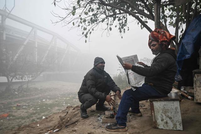 People sit near the Yamuna River amid dense smog during a winter morning in New Delhi on December 20, 2025. (Photo by Arun SANKAR / AFP)