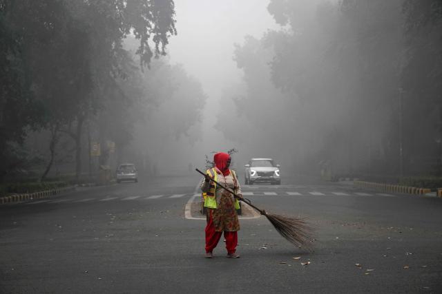 A civic worker sweeps a road amid dense smog during a winter morning in New Delhi on December 20, 2025. (Photo by Arun SANKAR / AFP)