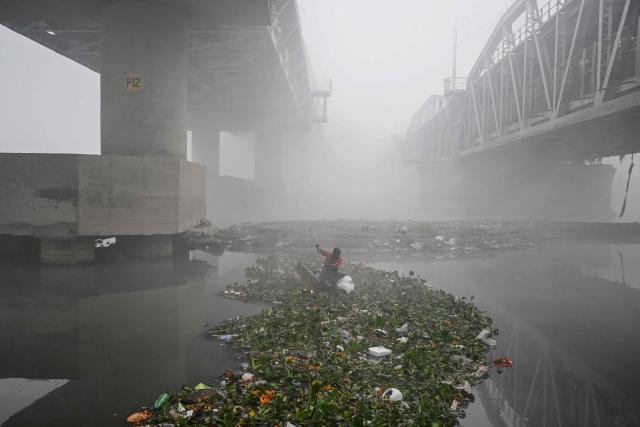 A man searches for usable items in the Yamuna River amid dense smog in New Delhi on December 20, 2025. (Photo by Arun SANKAR / AFP)