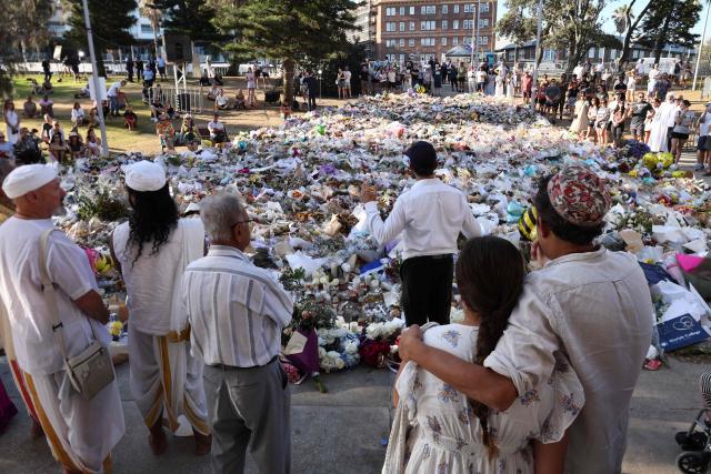A rabbi (centre R) delivers a sermon as mourners gather in front of tributes laid in memory of victims of a shooting at Bondi Beach, in Sydney on December 20, 2025. Father-and-son gunmen are accused of firing into crowds at a beachside Jewish festival on December 14, killing 15 in an attack authorities linked to "Islamic State ideology". (Photo by DAVID GRAY / AFP)
