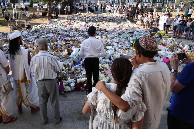 A rabbi (C) delivers a sermon as mourners gather in front of tributes laid in memory of victims of a shooting at Bondi Beach, in Sydney on December 20, 2025. Father-and-son gunmen are accused of firing into crowds at a beachside Jewish festival on December 14, killing 15 in an attack authorities linked to "Islamic State ideology". (Photo by DAVID GRAY / AFP)