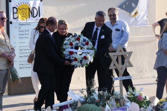 Officials from the Australian-Turkish community lay a wreath as mourners gather in front of tributes in memory of victims of a shooting at Bondi Beach, in Sydney on December 20, 2025. Father-and-son gunmen are accused of firing into crowds at a beachside Jewish festival on December 14, killing 15 in an attack authorities linked to "Islamic State ideology". (Photo by DAVID GRAY / AFP)