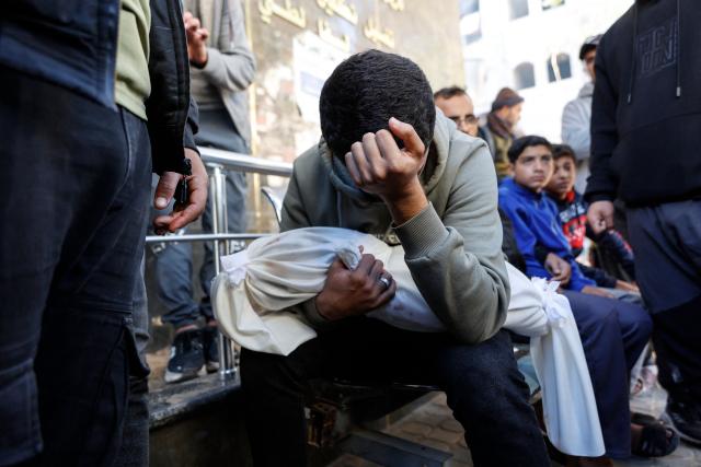 A Palestinian man carries the body of his 5-month-old brother, Ahmed Al-Nader, who was reportedly killed the previous day along with other family members in an Israeli shelling on a school-turned-shelter in the Tuffah neighbourhood of Gaza City, ahead of his funeral on December 20, 2025. Gaza's civil defence agency said Israeli shelling on a school-turned-shelter killed five people on December 19, 2025, while the military said it had fired at "suspicious individuals". The ceasefire that came into effect on October 10 has halted the fighting between Israel and Hamas, but it remains fragile with each side accusing the other of violating its terms. (Photo by Omar AL-QATTAA / AFP)