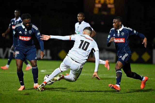 Paris FC’s French forward #07 Jonathan Ikone (L) and Paris FC’s  French midfielder #08 Adama Camara (R) fight for the ball with Raon-l’Etape’s French forward #10 Omar Hassidou (C) during the French Cup round of 64 football match between Raon l’Etape and Paris FC at the Paul-Gasser Stadium, in Raon-l'Etape, eastern France, on December 20, 2025. (Photo by Jean-Christophe VERHAEGEN / AFP)