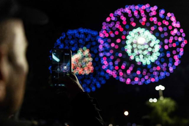 TOPSHOT - A man takes a photograph of fireworks during the celebrations of Saint Lucy in Syracuse, Sicily, southern Italy on December 20, 2025. Syracuse marked the feast of its patron saint with religious ceremonies, public gatherings and a fireworks display illuminating the historic waterfront. (Photo by Sameer Al-DOUMY / AFP)