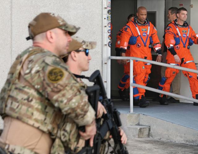 NASA Astronaut and Artemis II pilot Victor Glover (left) glances toward NASA Protective Service policemen while departing the Neil A. Armstrong Operations and Checkout Building at the Kennedy Space Center in Cape Canaveral, Florida on December 20, 2025. Alongside Glover is NASA astronaut and Artemis II Commander Reid Wiseman. The pair and fellow crew members Canadian Space Agency astronaut and Mission Specialist Jeremy Hansen and NASA astronaut and NASA astronaut and Mission Specialist Christina Koch performed a Countdown Demonstration Test on Saturday. Designed to test launch-day procedures, the test is a dress rehearsal of what will happen on launch day, which is currently targeted for no earlier than February 1, 2026. (Photo by Gregg Newton / AFP)