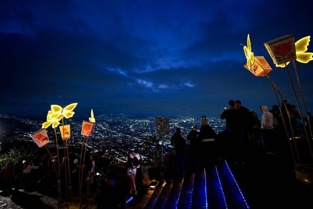 People observe the city near traditional Christmas lights at the Monserrate Mountain in Bogota on December 20, 2025. (Photo by Pablo VERA / AFP)