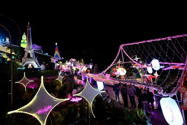 People walk past traditional Christmas lights at the Monserrate Mountain in Bogota on December 20, 2025. (Photo by Pablo VERA / AFP)
