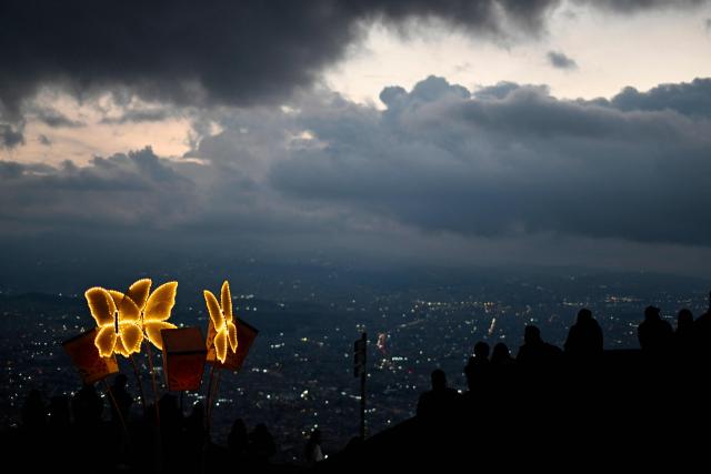 People observe the city near traditional Christmas lights at the Monserrate Mountain in Bogota on December 20, 2025. (Photo by Pablo VERA / AFP)