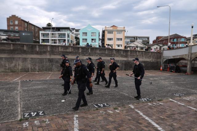 Police officers patrol before a memorial near a small bridge where gunmen had stood during a mass shooting in Bondi Beach, in Sydney on December 21, 2025. (Photo by DAVID GRAY / AFP)