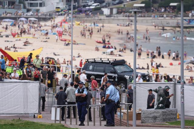 Police officers stand ahead of a memorial for the victims of a shooting at Bondi Beach in Sydney on December 21, 2025. (Photo by DAVID GRAY / AFP)