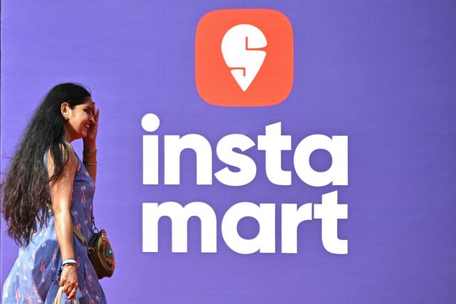 A woman walks past an advertisement of Indian quick-commerce platform Swiggy’s Instamart in Bengaluru on December 21, 2025. commerce (Photo by Idrees MOHAMMED / AFP)