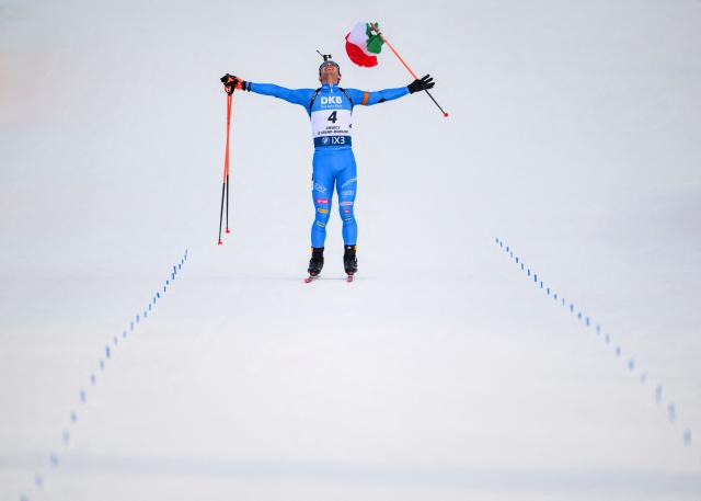 Italy's Tommaso Giacomel skies to the finish line with an Italian flag celebrating his win during the men's 15km mass start event of the IBU Biathlon World Cup, in Le Grand Bornand, near Annecy, southeastern France, on December 21, 2025. (Photo by Olivier CHASSIGNOLE / AFP)
