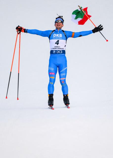 Italy's Tommaso Giacomel skies to the finish line with an Italian flag celebrating his win during the men's 15km mass start event of the IBU Biathlon World Cup, in Le Grand Bornand, near Annecy, southeastern France, on December 21, 2025. (Photo by Olivier CHASSIGNOLE / AFP)