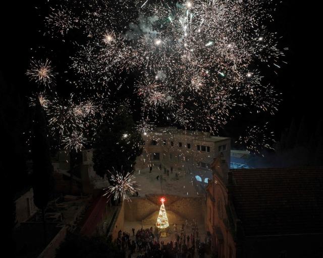 Fireworks light the night sky as residents gather in front of a Christmas tree for the start of  Christmas festivities in the mainly Christian village of Al-Qanayyah, northwest of Idlib on December 14, 2025. During the 14-year Syria civil war, the Islamic Jihadist groups were active in this area of northwest Syria forcing many of the local Christian community to abandoned their towns and villages settling mainly in former president Bashar al-Assad regime-controlled areas. (Photo by Omar HAJ KADOUR / AFP)