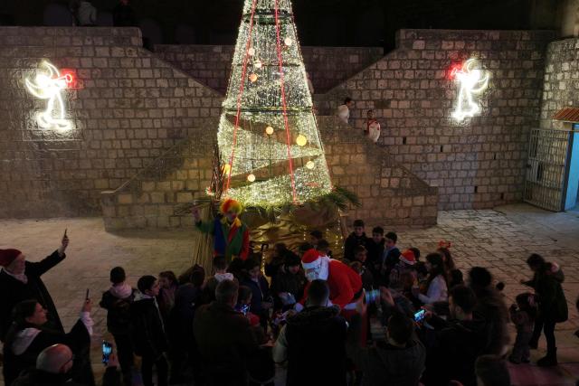 Residents gather in front of a Christmas tree as Santa Claus speaks to the children at the start of  Christmas festivities in the mainly Christian village of Al-Qanayyah, northwest of Idlib on December 14, 2025. During the 14-year Syria civil war, the Islamic Jihadist groups were active in this area of northwest Syria forcing many of the local Christian community to abandoned their towns and villages settling mainly in former president Bashar al-Assad regime-controlled areas. (Photo by Omar HAJ KADOUR / AFP)