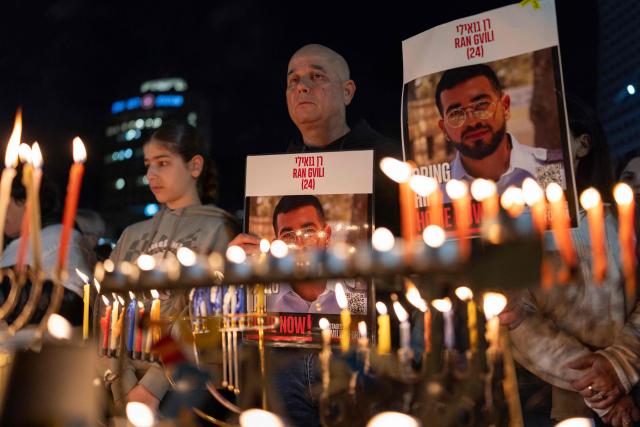 Israelis light the 8th candle of Hannukah in Hostage Square holding placards bearing the face of Ran Gvili in Tel Aviv on December 21, 2025, as they call for the return of his remains. Of the 251 people taken hostage during Hamas's unprecedented October 7, 2023 attack that sparked the war in Gaza, all but the remains of Israeli Ran Gvili have been handed over. (Photo by ILIA YEFIMOVICH / AFP)
