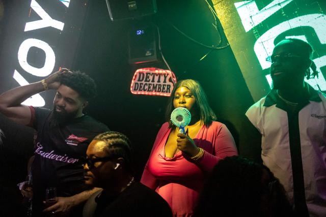 A patron uses a fan next to a sign that reads "Detty December" inside the Voyage nightclub in Ikeja in Lagos on December 7, 2025. “Detty December” refers to the lively Lagos tradition where December is packed with nonstop parties, concerts, nightlife, and cultural events, fuelled by returning diaspora Nigerians and heightened local celebration. The city becomes especially vibrant and crowded as entertainment and tourism peak. The spelling “detty” comes from Nigerian Pidgin English, where it is a playful version of “dirty” that implies excess, intensity, and carefree fun. (Photo by OLYMPIA DE MAISMONT / AFP)