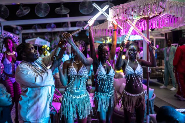 Waitresses hold fluorescent tubes as they prepare serve drinks to customers at the Lulu beach club during its opening during “Detty December” in Lagos on November 21, 2025. “Detty December” refers to the lively Lagos tradition where December is packed with nonstop parties, concerts, nightlife, and cultural events, fuelled by returning diaspora Nigerians and heightened local celebration. The city becomes especially vibrant and crowded as entertainment and tourism peak. The spelling “detty” comes from Nigerian Pidgin English, where it is a playful version of “dirty” that implies excess, intensity, and carefree fun. (Photo by OLYMPIA DE MAISMONT / AFP)