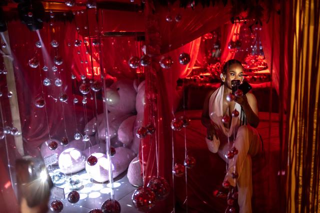 A patron uses a phone to take a photo on a bed in a decorated selfie space inside the restroom of the Lulu beach club during its opening during “Detty December” in Lagos on November 21, 2025. “Detty December” refers to the lively Lagos tradition where December is packed with nonstop parties, concerts, nightlife, and cultural events, fuelled by returning diaspora Nigerians and heightened local celebration. The city becomes especially vibrant and crowded as entertainment and tourism peak. The spelling “detty” comes from Nigerian Pidgin English, where it is a playful version of “dirty” that implies excess, intensity, and carefree fun. (Photo by OLYMPIA DE MAISMONT / AFP)