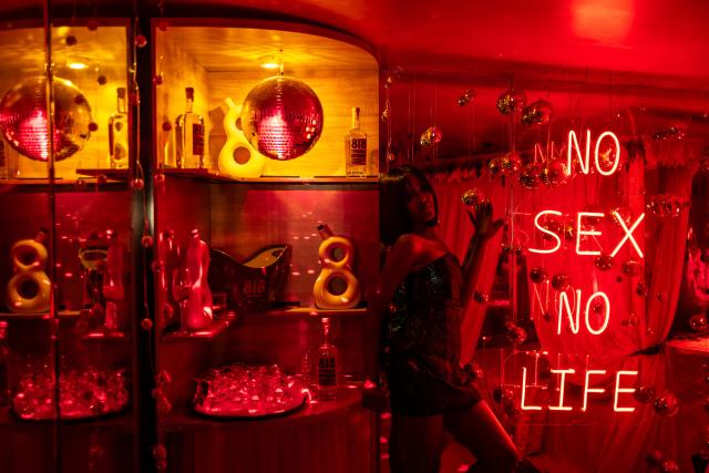 A patron poses for a photograph next to a bar and a fluorescent writing that reads 'no sex no life' in a decorated selfie space inside the restroom of the Lulu beach club during its opening during “Detty December” in Lagos on November 21, 2025. “Detty December” refers to the lively Lagos tradition where December is packed with nonstop parties, concerts, nightlife, and cultural events, fuelled by returning diaspora Nigerians and heightened local celebration. The city becomes especially vibrant and crowded as entertainment and tourism peak. The spelling “detty” comes from Nigerian Pidgin English, where it is a playful version of “dirty” that implies excess, intensity, and carefree fun. (Photo by OLYMPIA DE MAISMONT / AFP)
