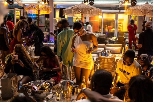 Patrons stand and dance inside the Lulu beach club during its opening during “Detty December” in Lagos on November 22, 2025. “Detty December” refers to the lively Lagos tradition where December is packed with nonstop parties, concerts, nightlife, and cultural events, fuelled by returning diaspora Nigerians and heightened local celebration. The city becomes especially vibrant and crowded as entertainment and tourism peak. The spelling “detty” comes from Nigerian Pidgin English, where it is a playful version of “dirty” that implies excess, intensity, and carefree fun. (Photo by OLYMPIA DE MAISMONT / AFP)