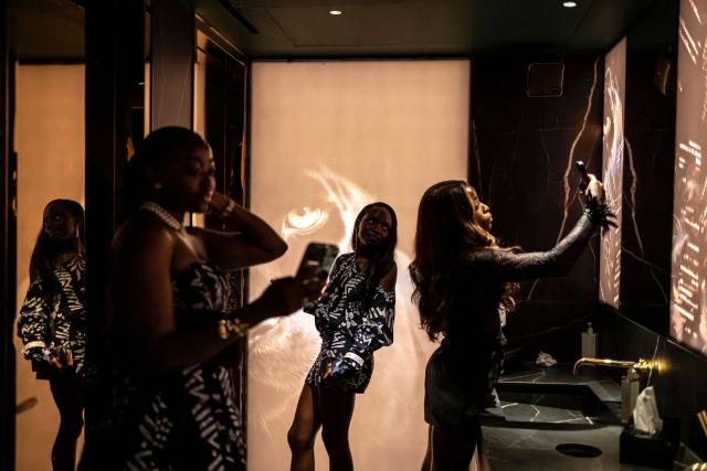 Patrons use their phones to take photos inside the restroom at the Mr. Panther restaurant and lounge during “Detty December” in Lagos on November 30, 2025. “Detty December” refers to the lively Lagos tradition where December is packed with nonstop parties, concerts, nightlife, and cultural events, fuelled by returning diaspora Nigerians and heightened local celebration. The city becomes especially vibrant and crowded as entertainment and tourism peak. The spelling “detty” comes from Nigerian Pidgin English, where it is a playful version of “dirty” that implies excess, intensity, and carefree fun. (Photo by OLYMPIA DE MAISMONT / AFP)