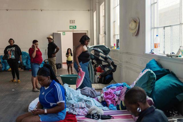Residents walk through one of the main halls of an occupied in downtown Cape Town on December 18, 2025. Nestled between spectacular mountains and the Atlantic Ocean, Cape Town has emerged as a growing tourism destination, topping in 2025 the Telegraph and Time Out magazine's rankings of best cities in the world. 
Activists say the drive to profit from tourism accommodation is pricing locals out of coveted neighbourhoods, including areas near District Six -- a site long associated with the apartheid-era removals that displaced non-white communities to remote, underdeveloped townships. (Photo by GIANLUIGI GUERCIA / AFP)