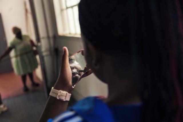 A girl applies make up in one in one of the halls of an occupied building in downtown Cape Town on December 18, 2025. Nestled between spectacular mountains and the Atlantic Ocean, Cape Town has emerged as a growing tourism destination, topping in 2025 the Telegraph and Time Out magazine's rankings of best cities in the world. 
Activists say the drive to profit from tourism accommodation is pricing locals out of coveted neighbourhoods, including areas near District Six -- a site long associated with the apartheid-era removals that displaced non-white communities to remote, underdeveloped townships. (Photo by GIANLUIGI GUERCIA / AFP)