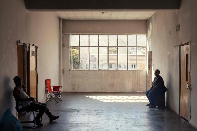 Two residents sit in a lobby at the first floor of an occupied building in downtown Cape Town on December 18, 2025. Nestled between spectacular mountains and the Atlantic Ocean, Cape Town has emerged as a growing tourism destination, topping in 2025 the Telegraph and Time Out magazine's rankings of best cities in the world. 
Activists say the drive to profit from tourism accommodation is pricing locals out of coveted neighbourhoods, including areas near District Six -- a site long associated with the apartheid-era removals that displaced non-white communities to remote, underdeveloped townships. (Photo by GIANLUIGI GUERCIA / AFP)