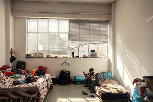 Children sit on a bed in one of the spaces transformed in a living quarte inside an occupied building in downtown Cape Town on December 18, 2025. Nestled between spectacular mountains and the Atlantic Ocean, Cape Town has emerged as a growing tourism destination, topping in 2025 the Telegraph and Time Out magazine's rankings of best cities in the world. 
Activists say the drive to profit from tourism accommodation is pricing locals out of coveted neighbourhoods, including areas near District Six -- a site long associated with the apartheid-era removals that displaced non-white communities to remote, underdeveloped townships. (Photo by GIANLUIGI GUERCIA / AFP)