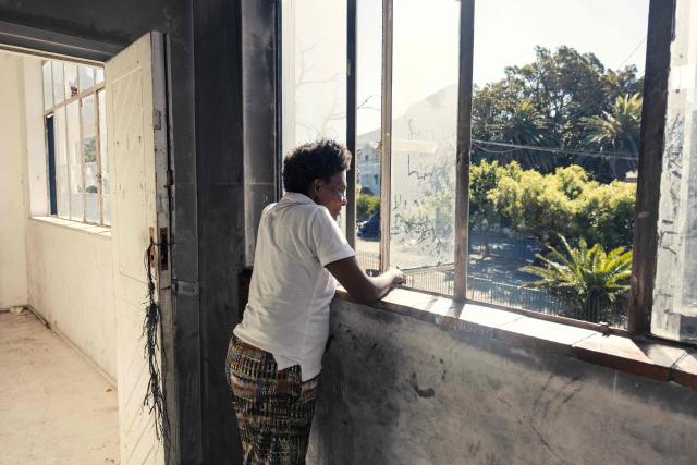 A resident looks out from a window of an occupied building in downtown Cape Town on December 18, 2025. Nestled between spectacular mountains and the Atlantic Ocean, Cape Town has emerged as a growing tourism destination, topping in 2025 the Telegraph and Time Out magazine's rankings of best cities in the world. 
Activists say the drive to profit from tourism accommodation is pricing locals out of coveted neighbourhoods, including areas near District Six -- a site long associated with the apartheid-era removals that displaced non-white communities to remote, underdeveloped townships. (Photo by GIANLUIGI GUERCIA / AFP)