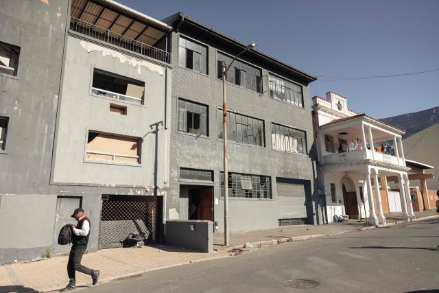 A security guard walks past an occupied building in downtown Cape Town on December 18, 2025. Nestled between spectacular mountains and the Atlantic Ocean, Cape Town has emerged as a growing tourism destination, topping in 2025 the Telegraph and Time Out magazine's rankings of best cities in the world. 
Activists say the drive to profit from tourism accommodation is pricing locals out of coveted neighbourhoods, including areas near District Six -- a site long associated with the apartheid-era removals that displaced non-white communities to remote, underdeveloped townships. (Photo by GIANLUIGI GUERCIA / AFP)