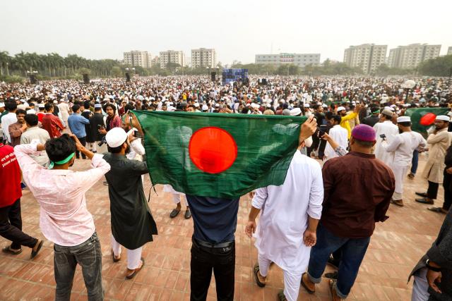 A mourner holds Bangladesh's national flag during the funeral of student leader Sharif Osman Hadi in Dhaka on December 20, 2025, after two days of violent protests over his killing. Huge crowds accompanied the funeral procession of Hadi, a key figure in last year's pro-democracy uprising who died in a hospital in Singapore on December 18 after being shot by masked gunmen while leaving a Dhaka mosque. (Photo by Niamul RIFAT / AFP)